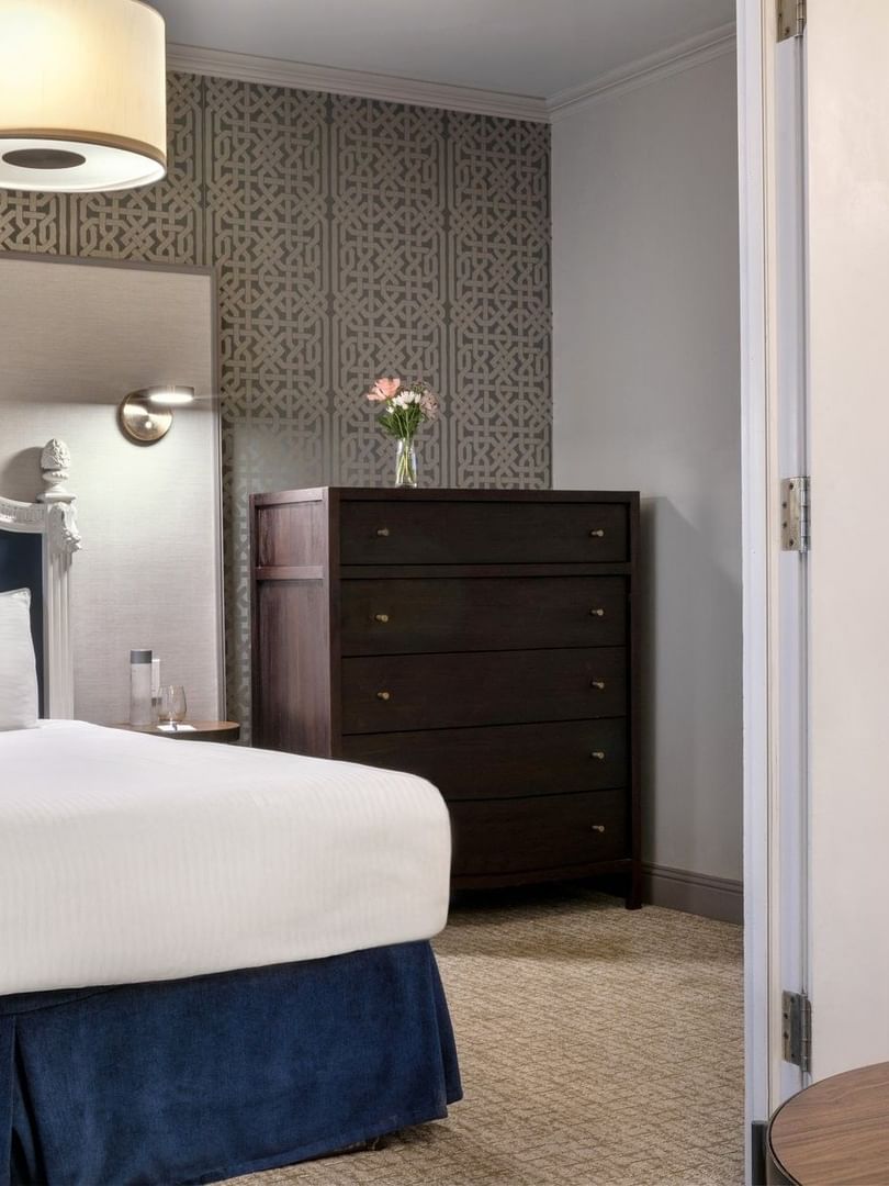 Dark wood dresser by a bed under a drum lamp near a white-framed doorway in Grand Suite at Warwick San Francisco