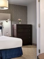 Dark wood dresser by a bed under a drum lamp near a white-framed doorway in Grand Suite at Warwick San Francisco