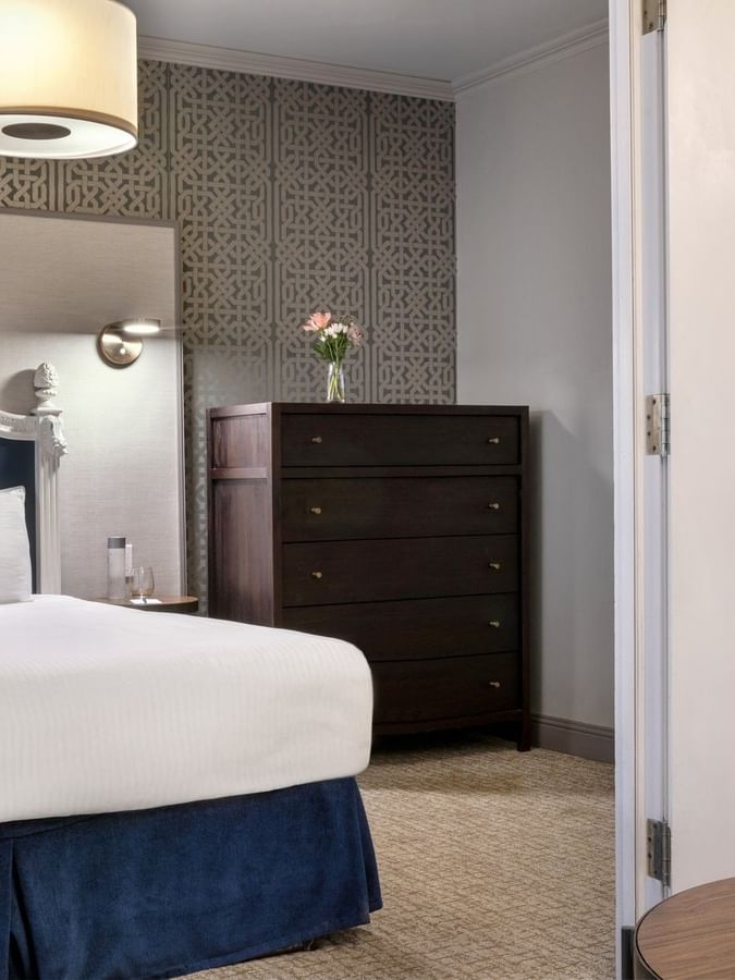 Dark wood dresser by a bed under a drum lamp near a white-framed doorway in Grand Suite at Warwick San Francisco