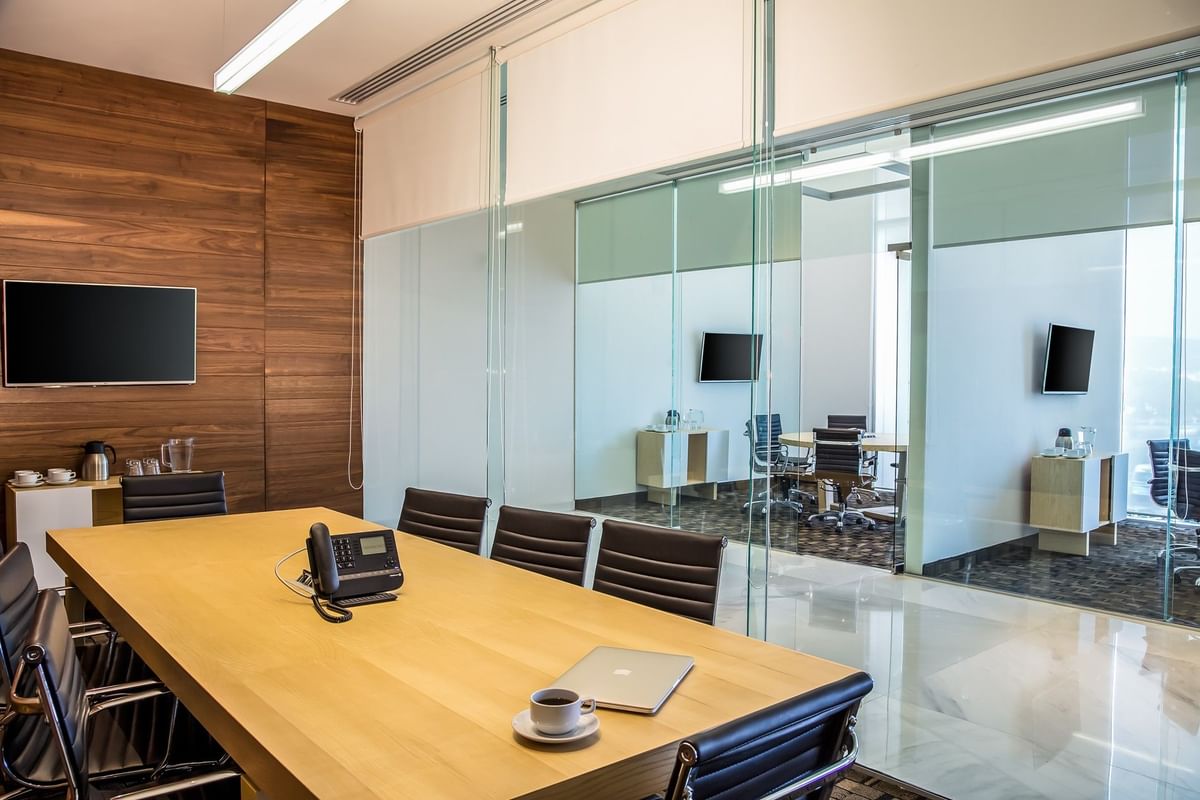 Sala de juntas elegante con mesa larga de madera, TV y divisores de vidrio en Fiesta Inn