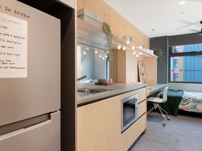 Compact apartment kitchen with microwave, sink, and fridge, leading to a bedroom at La Trobe University.