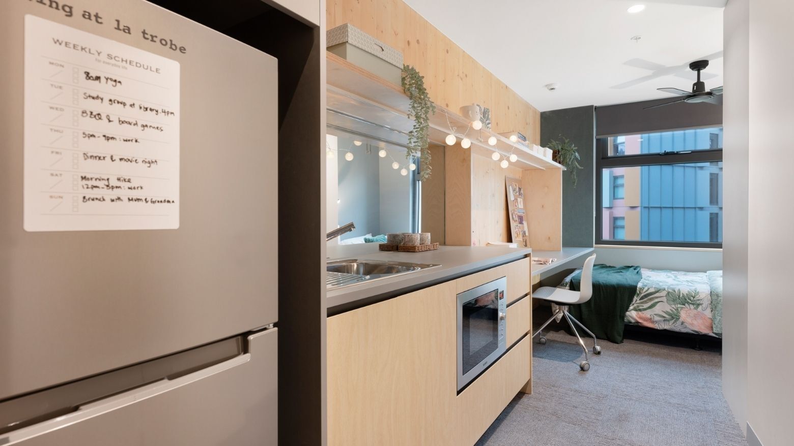 Compact apartment kitchen with microwave, sink, and fridge, leading to a bedroom at La Trobe University.