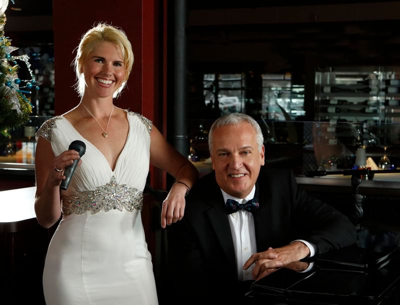Smiling female singer holding a microphone next to a male pianist in Chandler's Steakhouse at Hotel 43 Boise