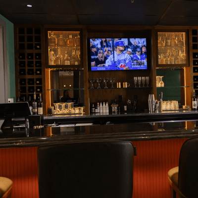 Bar counter with leather stools facing a mounted television screen displaying sports at La Tourelle Hotel and Spa