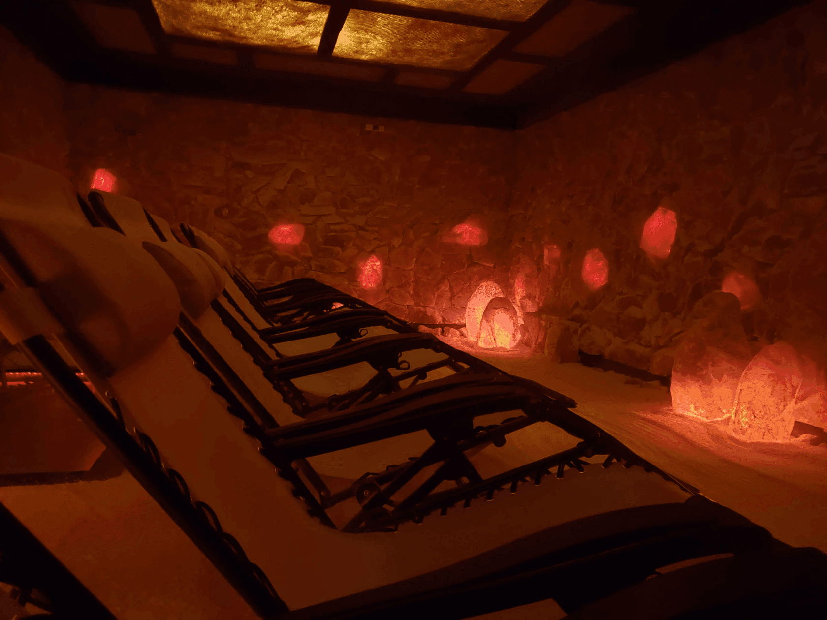 Empty salt lounge chairs with glowing red salt lamps glowing in a dimly lit room for relaxation.