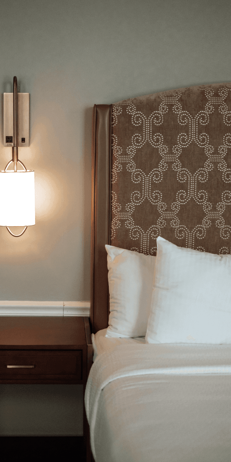 Wall sconce lamp glowing beside a patterned leather headboard with white pillows at La Tourelle Inn and Spa