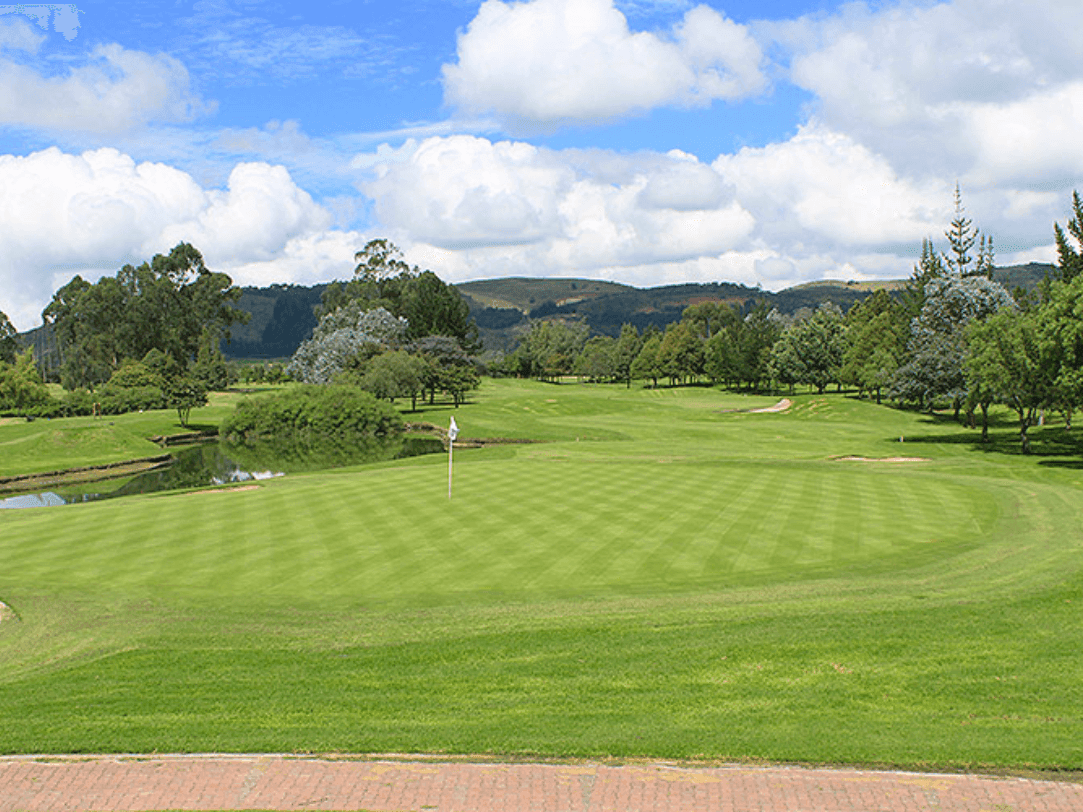 Vista panorámica de un extenso campo de golf con fairways verdes meticulosamente cuidados, suaves colinas, árboles y obstáculos de agua bajo un cielo azul brillante