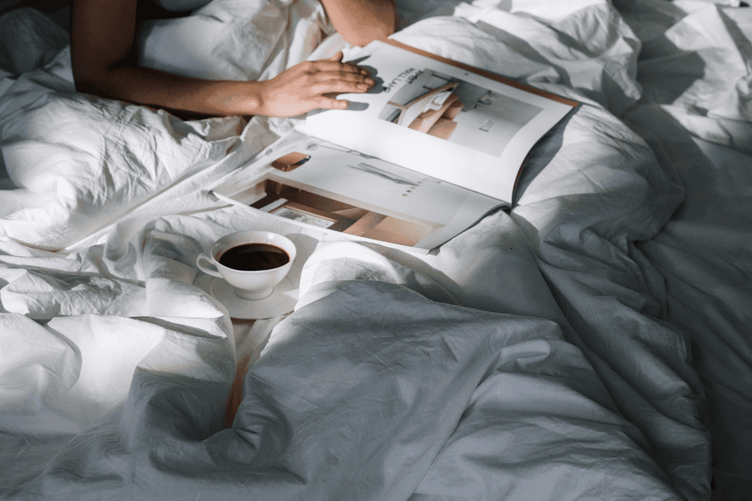 Man reading magazine & enjoying coffee on a bed at Amora Hotel