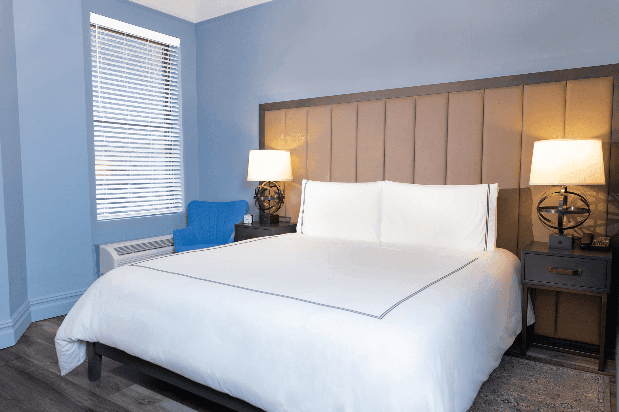 A wide view of a hotel room with a king-sized bed, two nightstands with lamps, and a window with blinds.