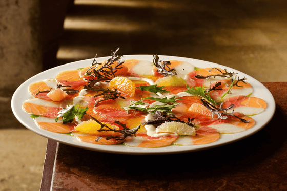 Carpaccio de pescado con cítricos y hierbas frescas en plato blanco en Hotel Charleston Santa Teresa