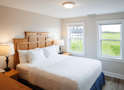 One-Bedroom Cottage with white king bed, wooden headboard, and golf course views at Rodd Crowbush Golf & Beach Resort