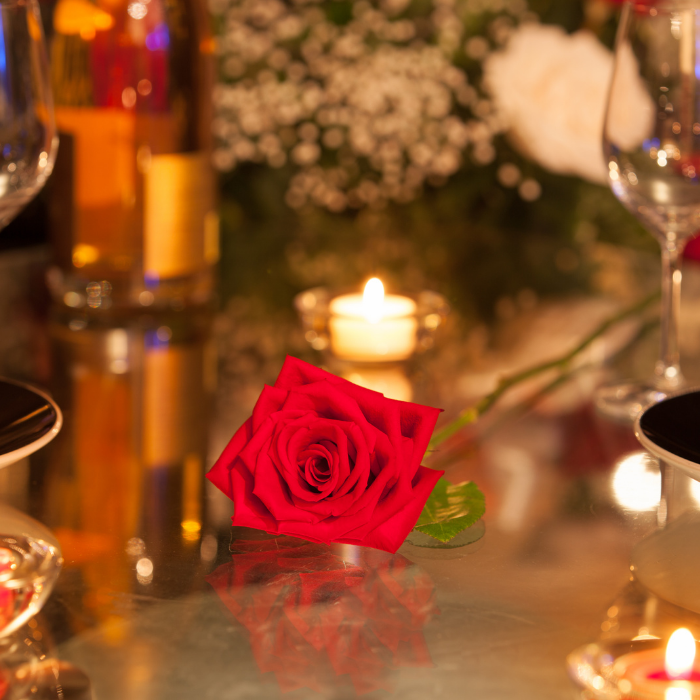close up of romantic Valentine's table setting with tea light candles, 2 wine glasses, and red rose