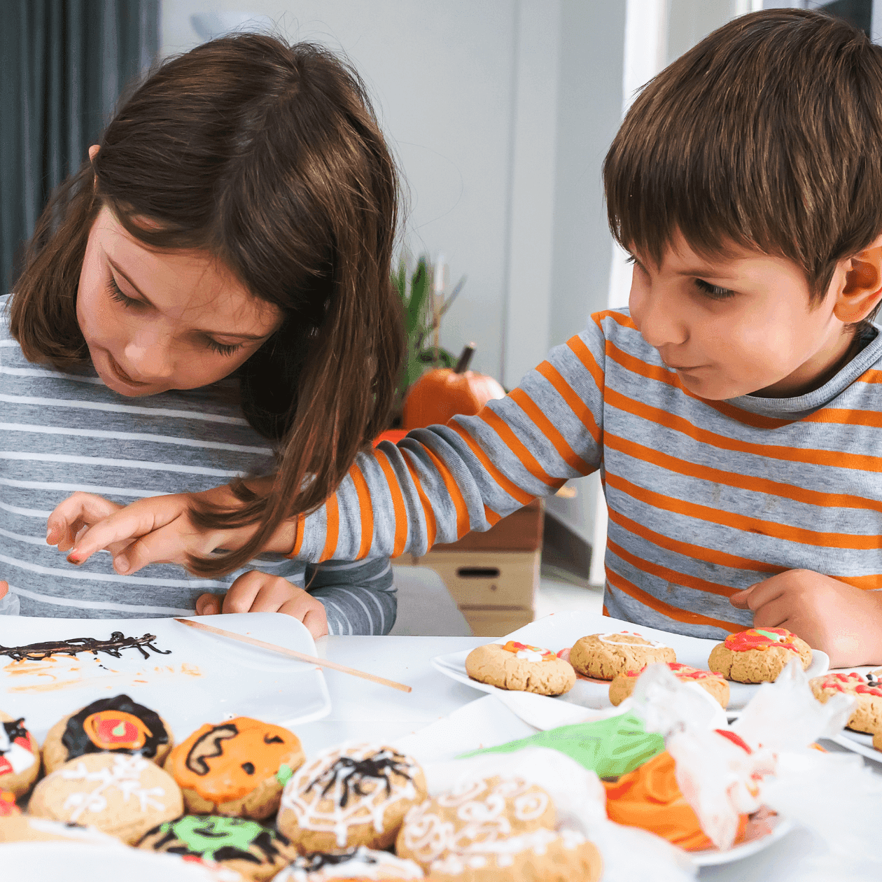 Two children decorating cookies with icing at a white table, enjoying a fall activity in Grand Summit Hotel at Attitash