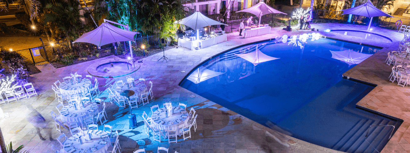 An outdoor pool with surrounding tables and chairs set up for an event at night.