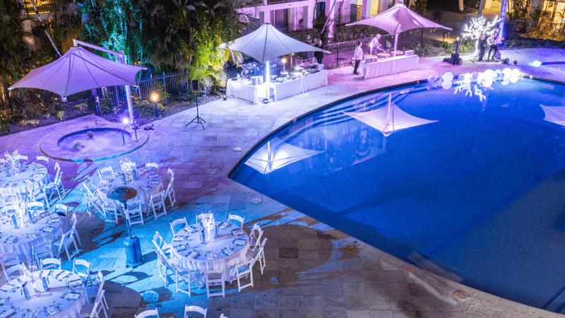 An outdoor pool with surrounding tables and chairs set up for an event at night.