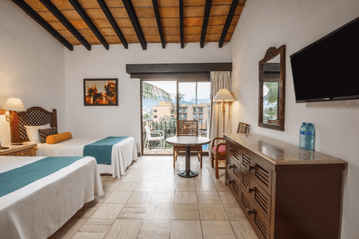 Hotel room with two beds, a table, chairs, a balcony, a dresser, a TV, and a mirror.
