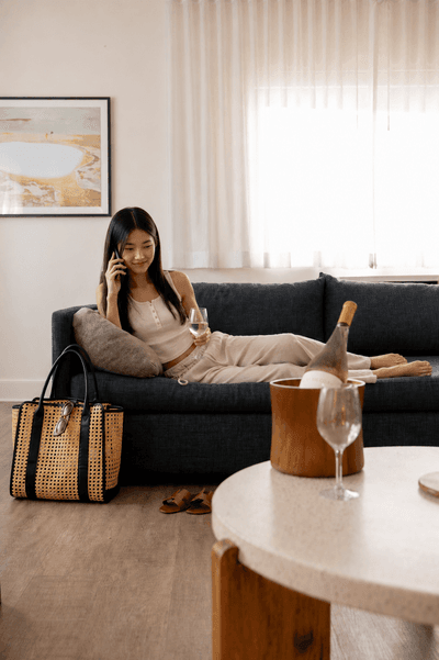 Woman relaxing on sofa with phone and wine in modern hotel suite at Kenmore Village Hotel, South Beach