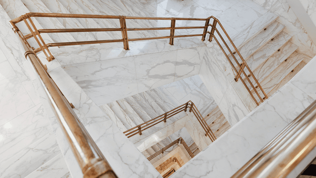 Marble staircase with gold railings spiraling downwards, showcasing an elegant design at Almanac X Alcron Prague