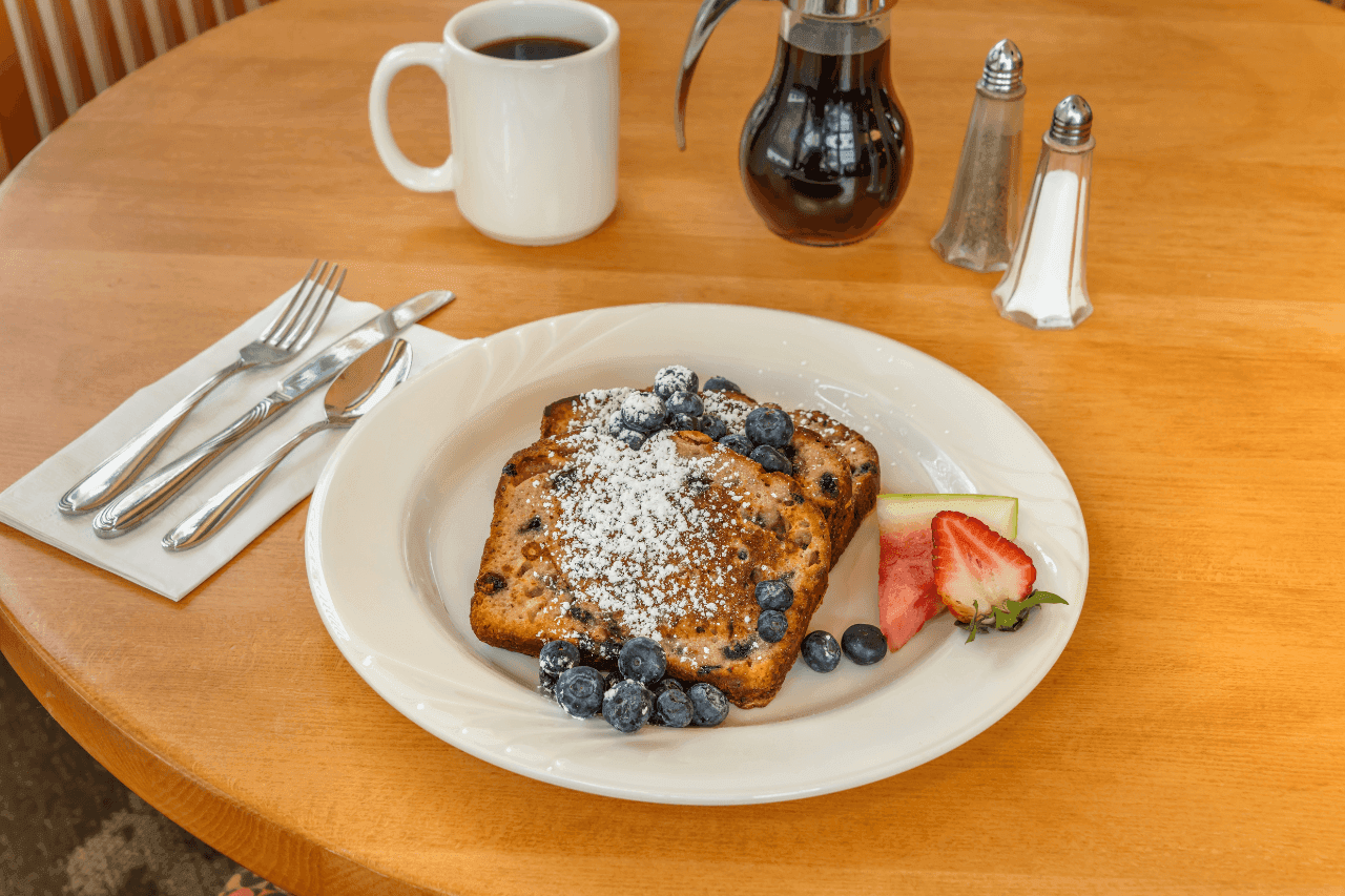 a plate of French toast with blueberries and strawberries on a wooden table