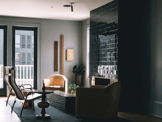 Modern living room with couches, side tables, potted plants, and a geometric tile wall.
