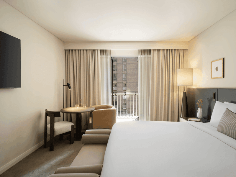 Modern hotel room with king bed, wooden desk area, armchair and large window with curtains