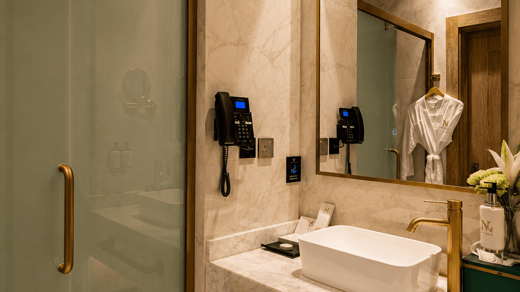 Sink below a mirror reflecting bathrobes in Deluxe Room at Naviti by Warwick Jeddah, capturing stylish hotel rooms in Jeddah