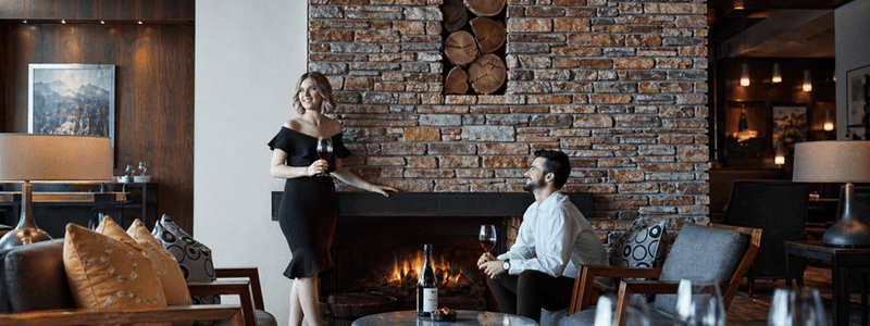 Couple enjoying wine in a cozy lounge with fireplace under offer Make Yourself at Home with Extended Winter Stays.
