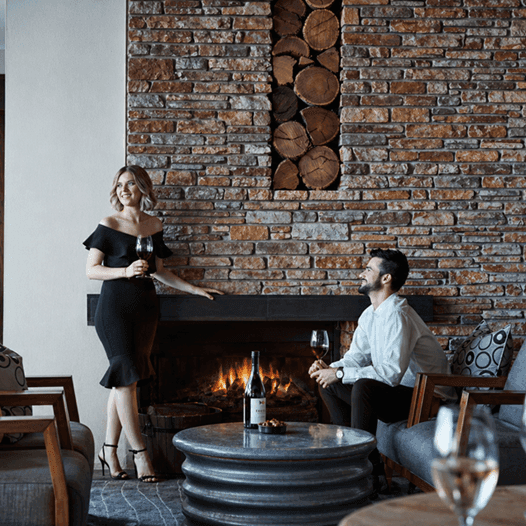 Couple enjoying wine in a cozy lounge with fireplace under offer Make Yourself at Home with Extended Winter Stays.