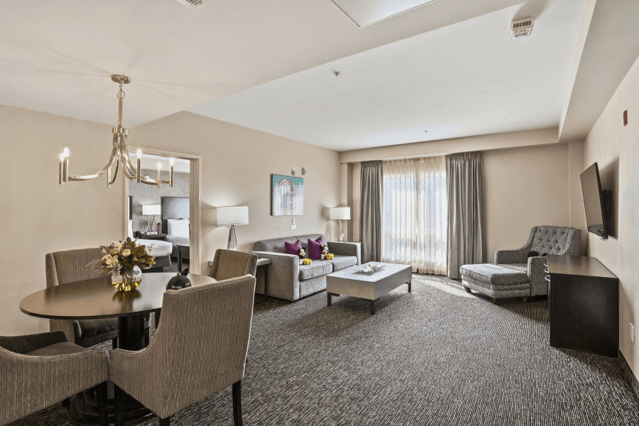 A wide view of a hotel suite with a living area, dining table, and doorway to another room.