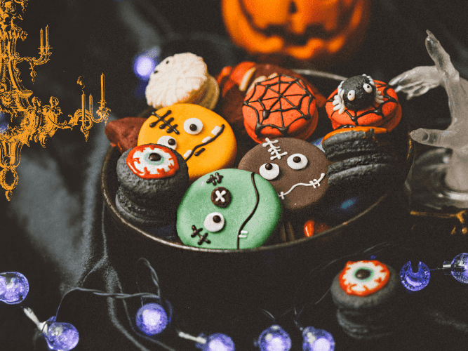  Festive Halloween cookies arranged beneath an elegant chandelier, featuring a whimsical spider for a spooky touch.