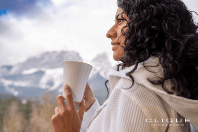 Woman in a white robe holds a mug, gazing at the majestic snow-capped mountains in the distance at Falcon Crest Lodge