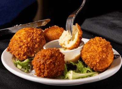 Golden fried potato croquettes on a plate with greens at Rodd Royalty, a gem for Charlottetown, PEI, restaurants