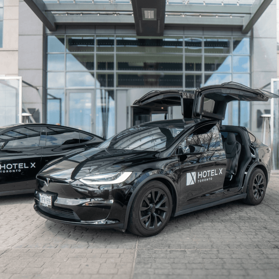 Black Tesla vehicles parked by the entrance at Hotel X Toronto, with one featuring open falcon-wing doors under a canopy