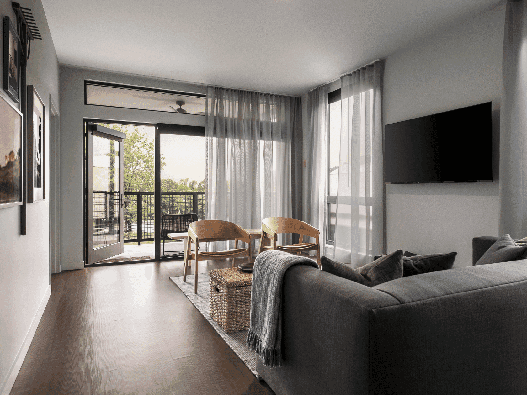 Living room with gray couch, two chairs, TV, balcony, and artwork on the wall.