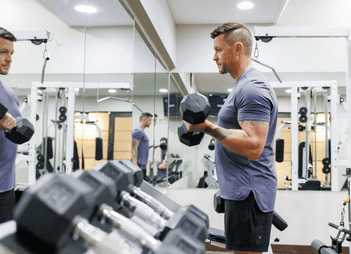 Man lifting weights in front of a mirror in fitness center at Rodd Royalty, one of the luxury hotels in Charlottetown, PEI