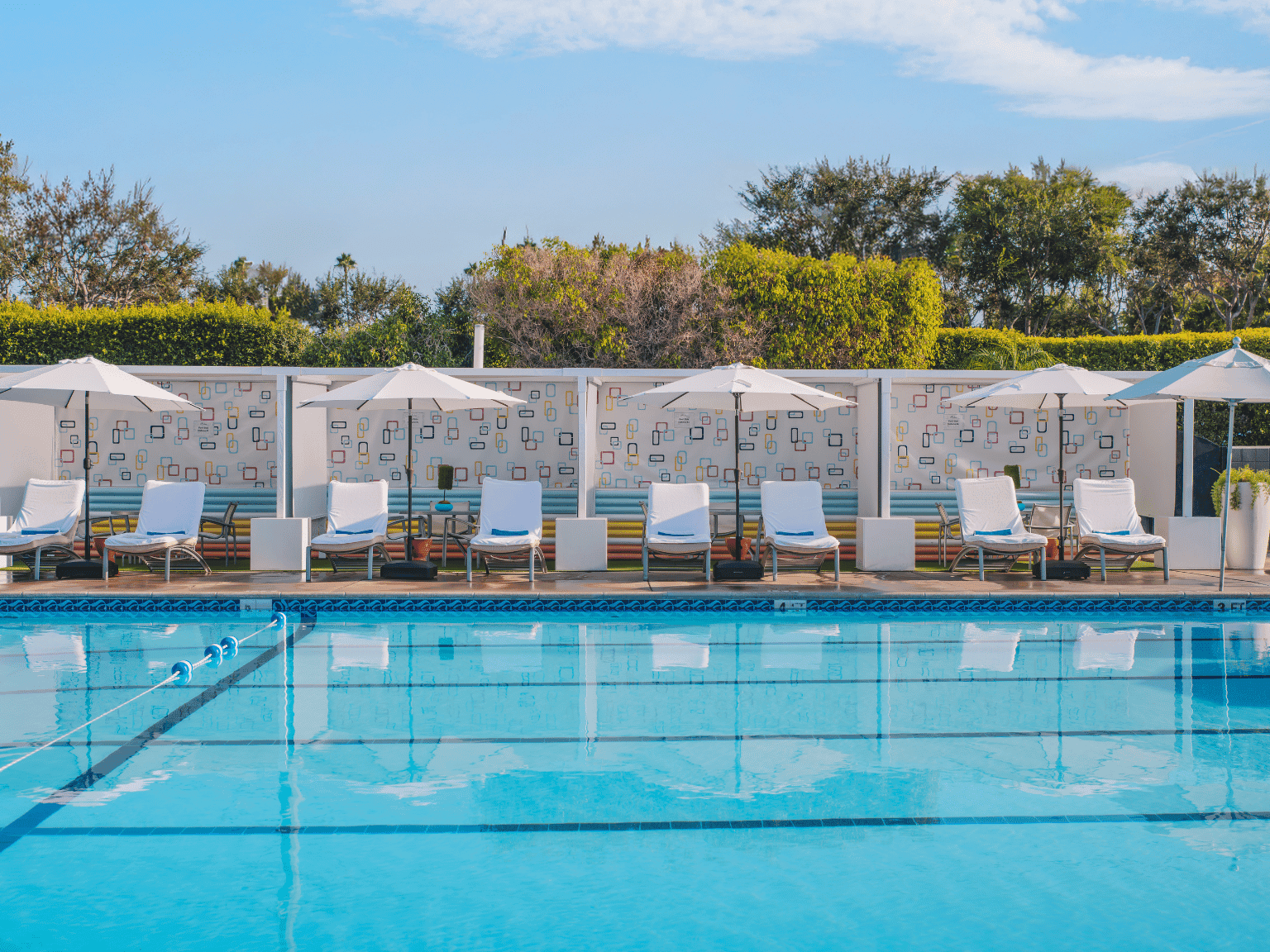 Outdoor pool with white lounge chairs and cabanas under a sunny sky at The Anaheim Hotel in Anaheim