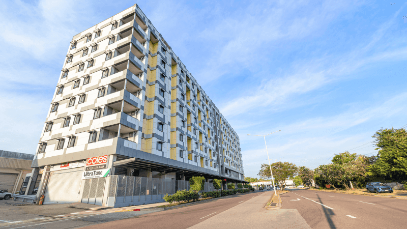 Modern apartment building with Coles and Ultra Tune storefronts on street corner.
