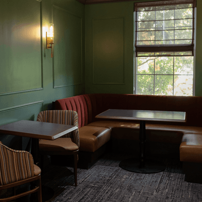 Green corner dining nook featuring a plush red leather booth and wooden tables at La Tourelle Hotel and Spa