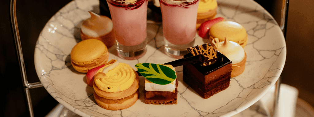 Two-tiered tray holding an array of desserts and drinks for Easter High Tea.