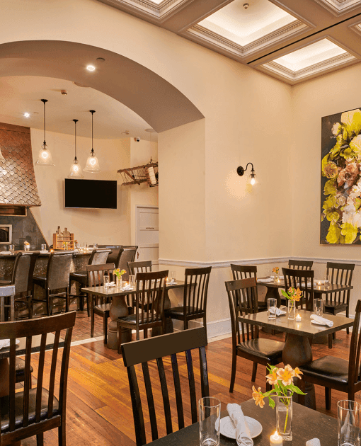 Wooden dining tables & chairs beside large floral painting with brick oven in Bistango at The Kimberly Hotel