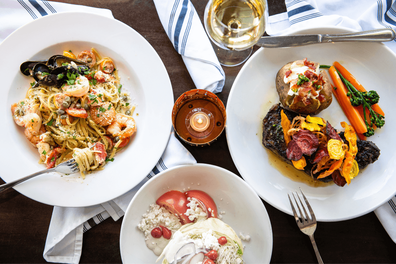 A table setting with three plates of food, a glass of white wine, and a candle.