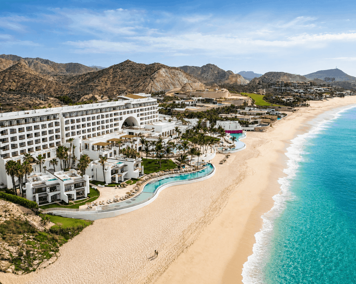 Aerial view of white beachfront resort with curved pool, palm trees, and turquoise ocean at Marquis Los Cabos Resort & Spa