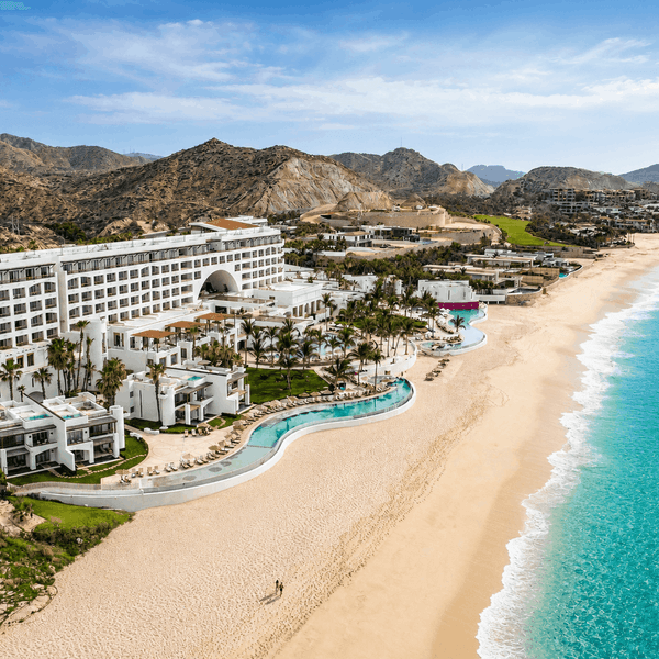 Aerial view of a beachfront resort with pools, palm trees, and turquoise ocean waters along a sandy shore.