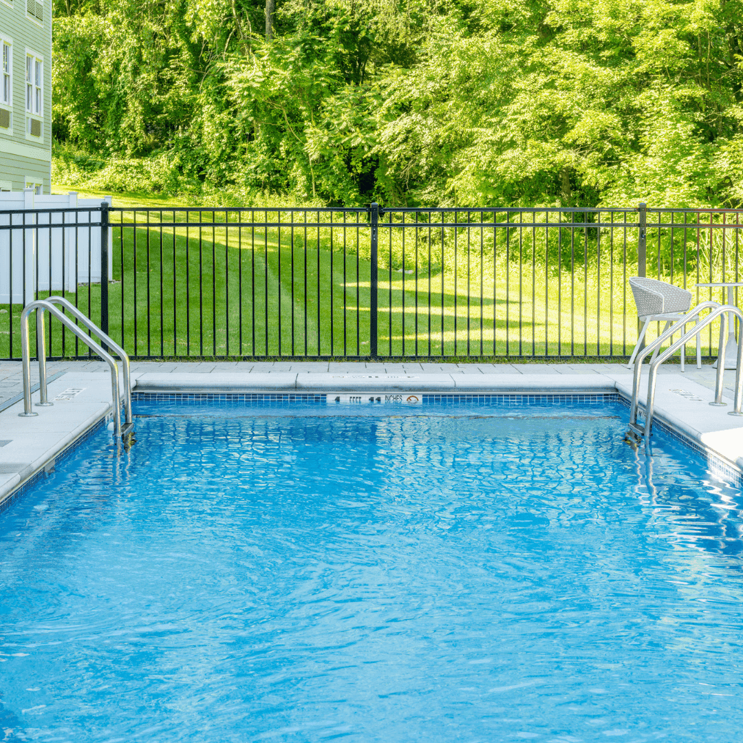 Empty outdoor pool with clear blue water, black fence, and a green lawn beyond.