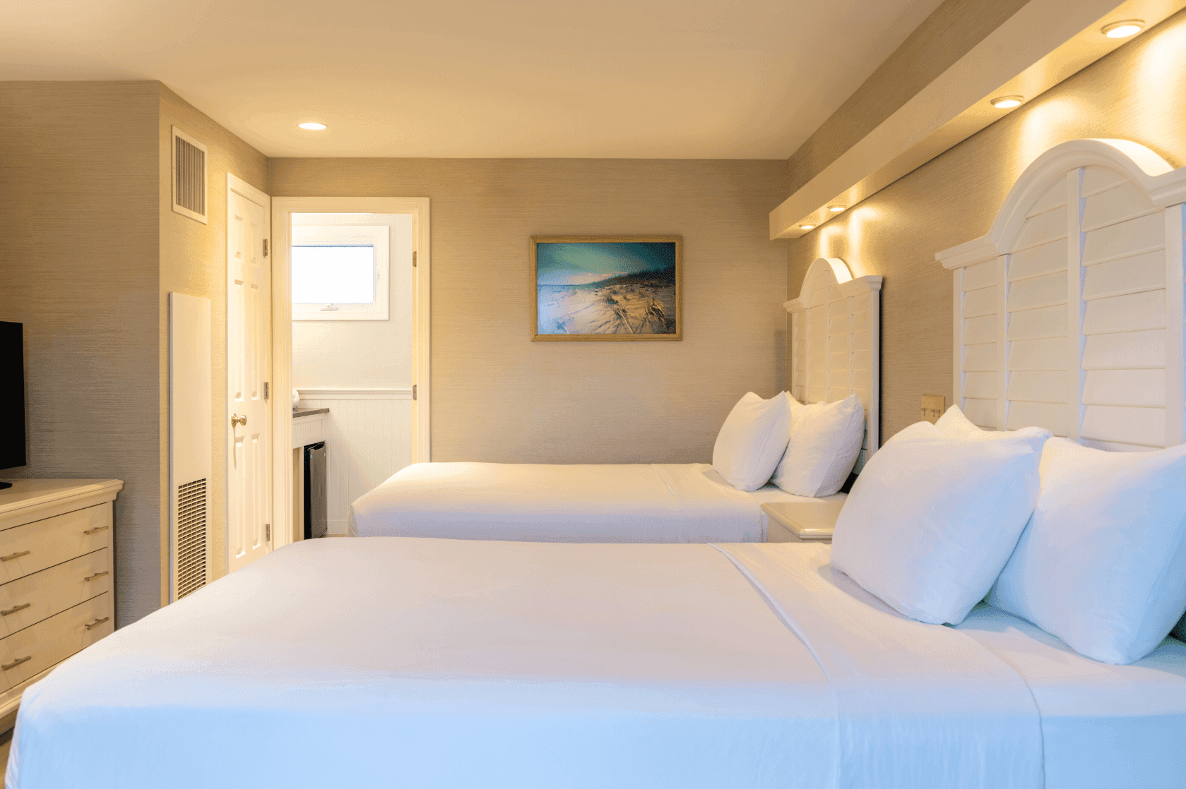 A hotel room with two double beds, beige walls, and white bedding