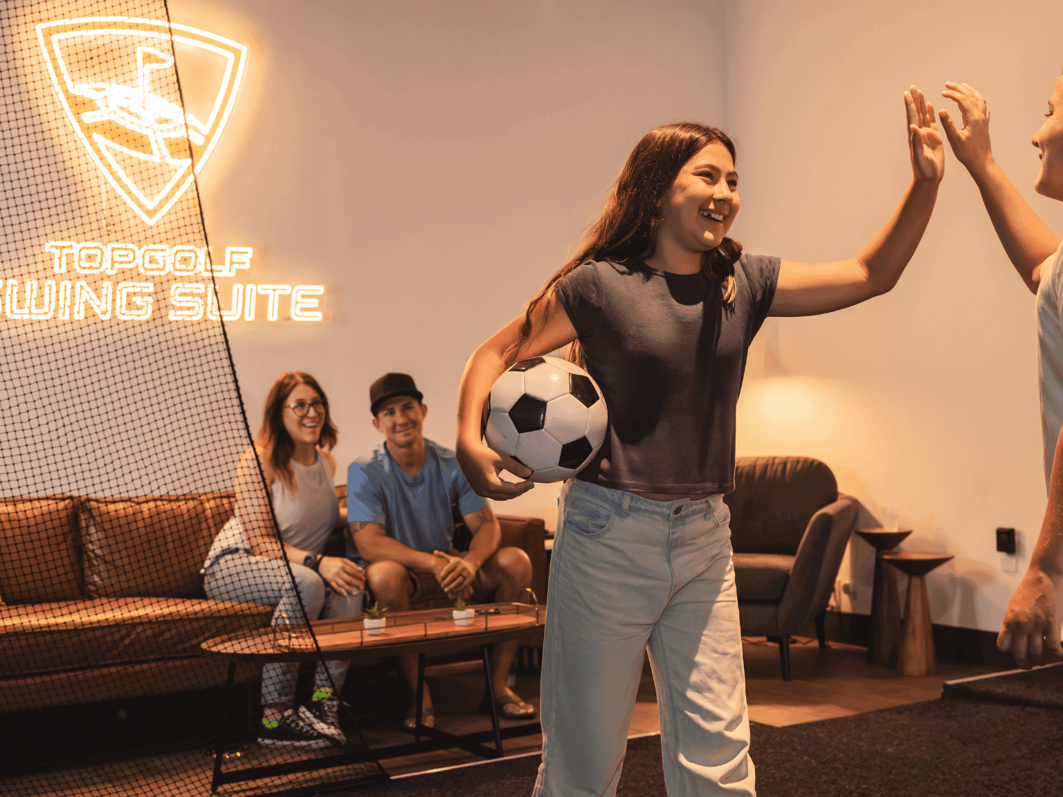 Two kids high fiving with parents smiling in the background at Anaheim Topgolf Swing Suite