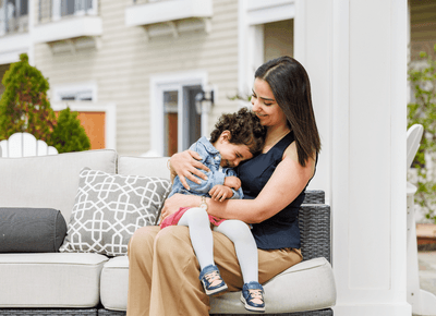 Mother cuddling her young child on a soft patio sofa beside patterned cushions at Rodd Crowbush Golf & Beach Resort