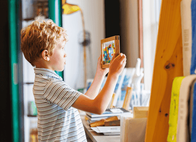 Young boy holding up a colorful framed artwork inside a bright and creative kids play activity area at Rodd Hotels & Resorts