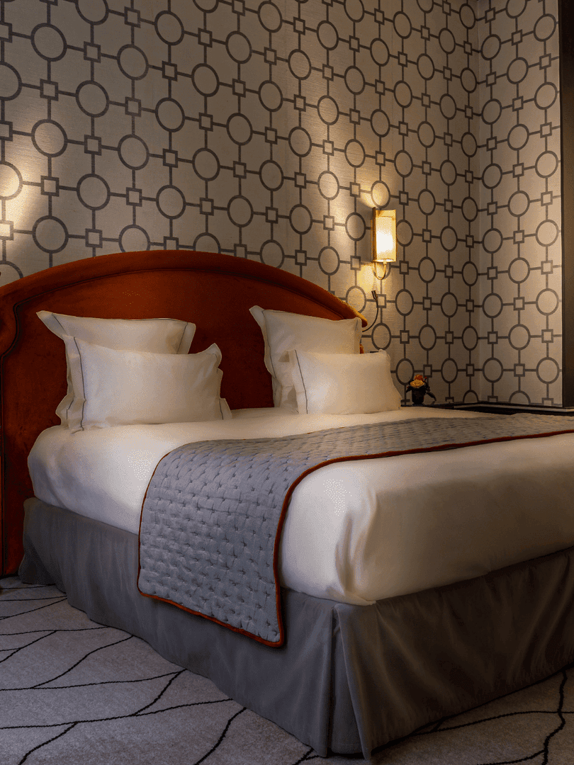 Bed with a side table set against a patterned wall in the Deluxe Suite Parisienne at Hotel Westminster Paris