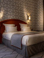 Bed with a side table set against a patterned wall in the Deluxe Suite Parisienne at Hotel Westminster Paris